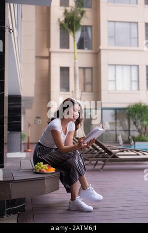 Woman reading a book near the water pool. Stock Photo