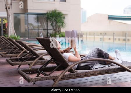 woman reading and relaxing near luxury swimming pool Stock Photo