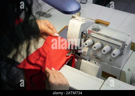 Young woman using professional overlock sewing machine in workshop. Equipment for edging, hemming or seaming clothes at tailors shop Stock Photo