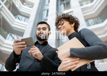 Below view of successful marketing specialists using smartphone while watching statistics on social media Stock Photo