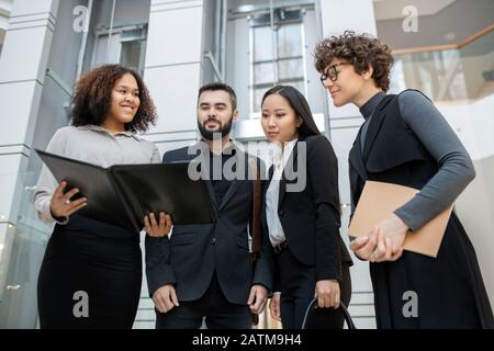 Smiling Afro-American manager holding open folder while presenting project plan to colleagues Stock Photo