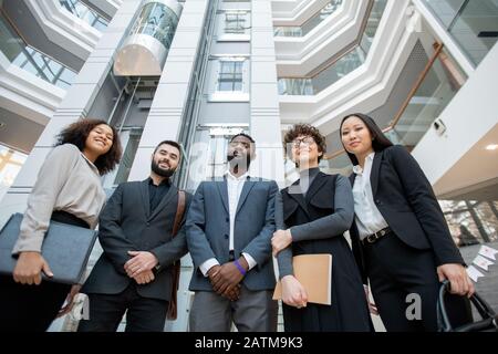Group of business specialists in formal outfits standing in semi-circular hall of office and looking at camera Stock Photo