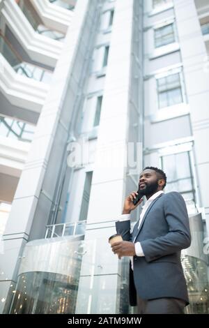 Below view of confident bearded businessman in suit drinking coffee and talking by phone while working on move Stock Photo