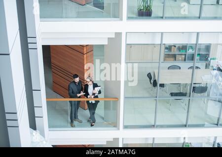 Above view of modern young business analysts standing at glassy railing and discussing report using tablet Stock Photo