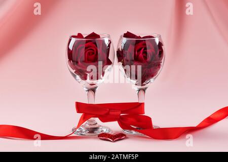 Two glasses of wine, rose and heart on a pink background. Valentines day card. Stock Photo