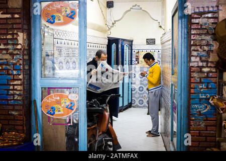 Men reading the newspaper and listening to music as the wait for phone booths in Marrakesh, Morocco Stock Photo