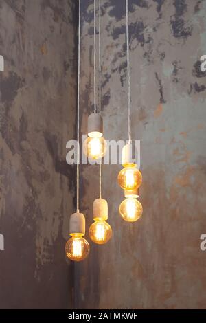 Many different vintage light bulbs hanging from ceiling. Loft pendant lamps on background of rough cement plaster on wall. Modern Edison light bulbs. Stock Photo