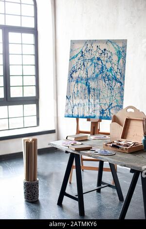 Easel, canvas, brushes, pencils, paints with albums on the table. The interior in the studio of the artist, workshop. Painting Studio of a freelance Stock Photo