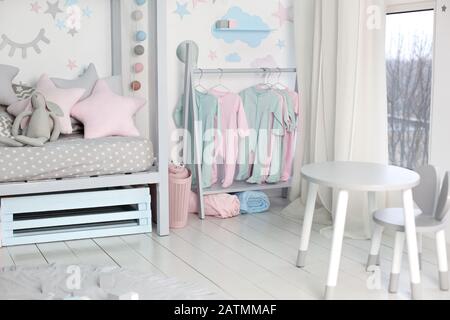 Clothes for little child hung in children room. Rack with hangers with baby clothes. Children cloth rack. Children's interior bedroom. Stock Photo