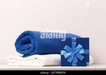 Close-up of a box with a gift of blue and white towels on a table against a background of light walls. Stock Photo