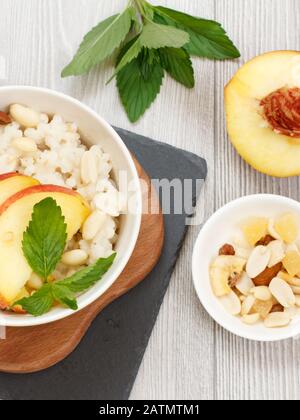 Sorghum porridge with pieces of peach, cashew nuts and almond in porcelain bowls, fresh peaches on wooden and stone boards. Vegan gluten-free sorghum Stock Photo
