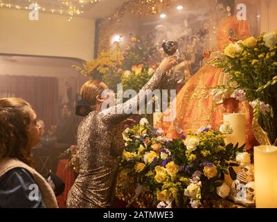 A trans priestess aims smoke at a statue of Santa Muerte in a home temple in Queens, New York City. Stock Photo