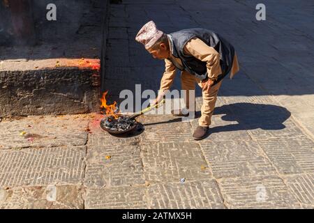 Kirtipur, Nepal - November 13, 2016: Nepali man kindles a ritual fire. Bagh Bhairab Temple. Stock Photo