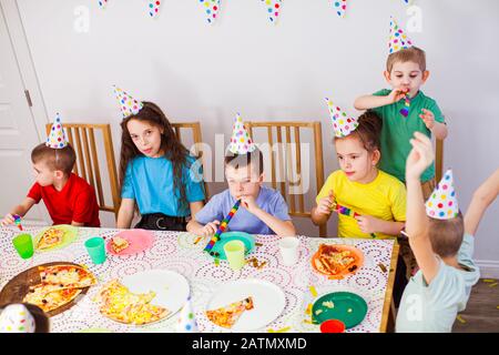 Kids celebrating a birthday with a pizza at cafe. Birthday party. Cute children in birthday hats having fun together Stock Photo