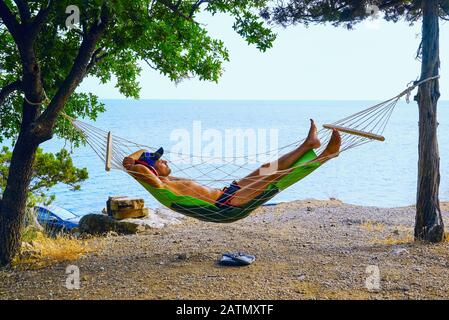 A young man is resting in a hammock on the beach Stock Photo