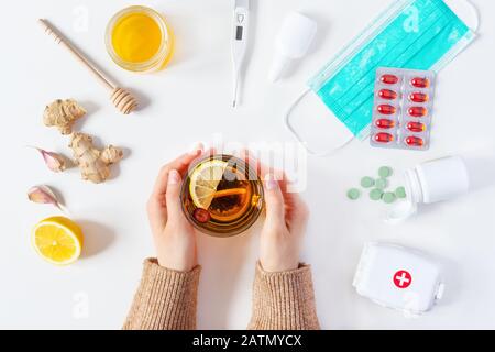 Composition of cold and flu treatments. Woman hands holding hot tea and different treatments around it. Medicaments and herbal medicine concept. Healt Stock Photo