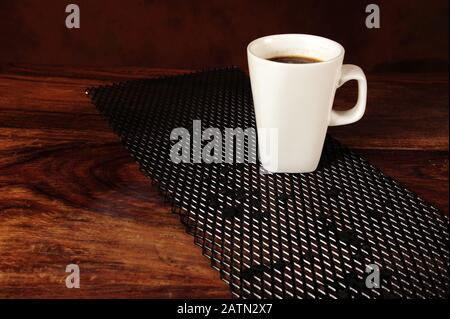 Black coffee in white on black diagonal metal grid with coffee beans. Old scratched wooden table surface. Stock Photo