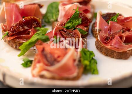 Sandwiches with prosciutto and sun-dried tomatoes on dark bread, spread with goat cheese. On a wooden background. Copy space Stock Photo