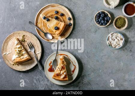 Pieces of cheesecake with different toppings on ceramic plates and variety of sauces in ceramic bowls over grey texture background. Flat lay, space Stock Photo