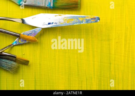 Artistic art supply utensils with paintbrushes on yellow canvas background with copy space flat lay top view from above Stock Photo