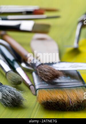Artistic art supply utensils with paintbrushes on yellow canvas background with selective focus Stock Photo