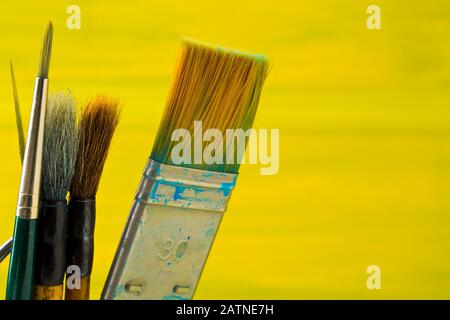 Artistic art supply utensils with paintbrushes on yellow canvas background with selective focus Stock Photo