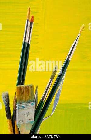 Artistic art supply utensils with paintbrushes on yellow canvas background with selective focus Stock Photo