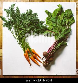 Heart shaped frame from fresh carrots and beetroots with greens tops on white background top view Stock Photo