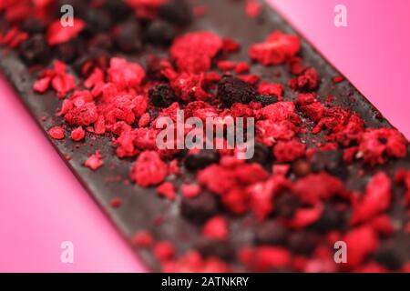 Dark low calorie chocolate with dried red berries on bright pink background, selective focus Stock Photo