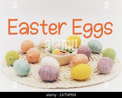 Easter Eggs on a round placemat surrounding a white ceramic bowl of pastel colored white chocolate mints with little white polka dots on a creamy back Stock Photo