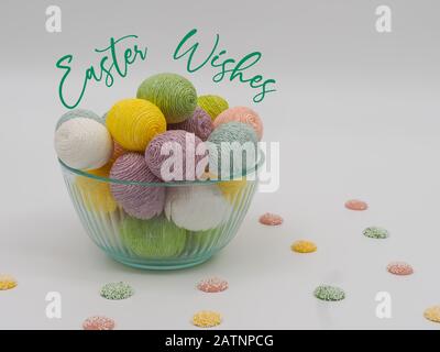 Easter Wishes in green cursive font on a white background with a glass bowl full of string decorated Easter eggs and pastel colored white chocolate ca Stock Photo
