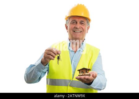 Old male builder with trustworthy expression holding small wooden house and keys isolated on white studio background Stock Photo