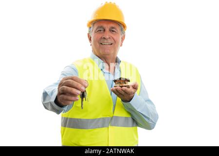 Old male architect smiling as showing keys and small wooden house as construction concept isolated on white background Stock Photo