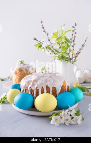 Easter cake, colorful blue and yellow eggs, fresh blooming flowers on light background. Close up. Vertical format Stock Photo