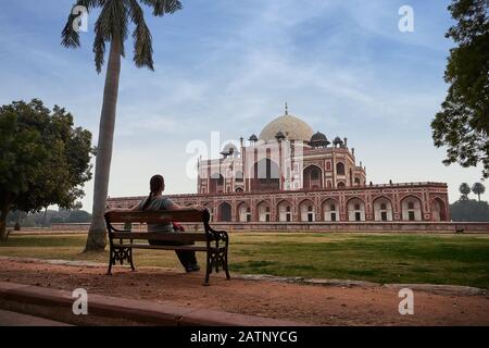 Young woman sitting at a bench and lookin to Humayun's tomb is the tomb of the Mughal Emperor Humayun in Delhi, India. Stock Photo