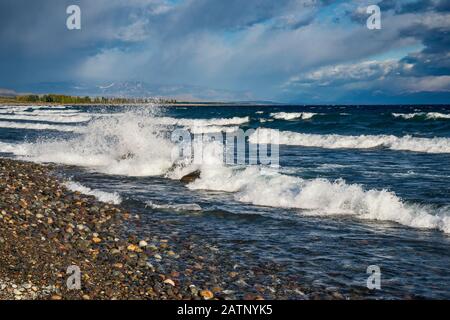 Waves breaking over rocks and pebbles at beach of Lago Buenos Aires aka Lago General Carrera, Andes mountains in far distance, Patagonia, Argentina Stock Photo