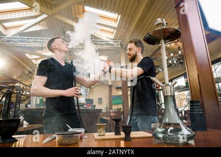 Hookah in the process preparation in cozy hookah bar. Two young men shisha masters giving five while preparing hookah for smoking. Stock Photo