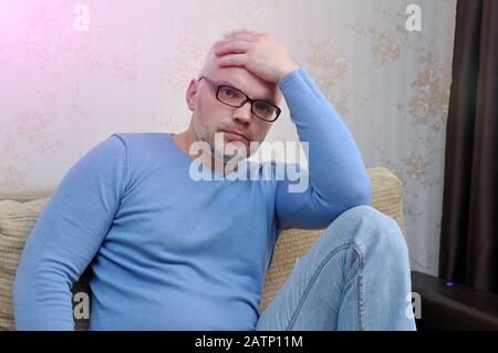 Young man in a blue sweater with a headache at home sitting on the couch Stock Photo