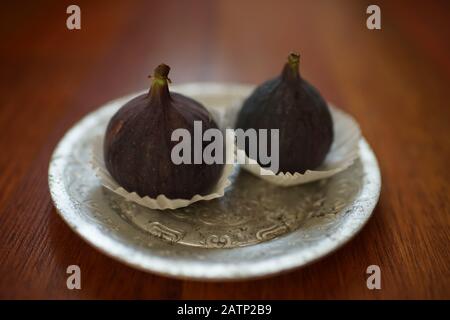 Two ripe sweet figs in silver plate on a wooden table Stock Photo