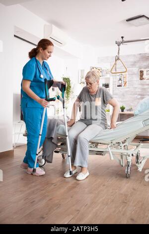 Caregiver in nursing home helping old woman to walk using crutches. Stock Photo