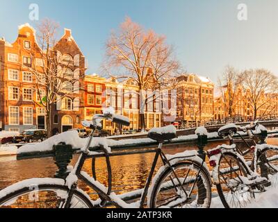 Bicycles covered with snow alongside a canal during winter in Amsterdam Stock Photo