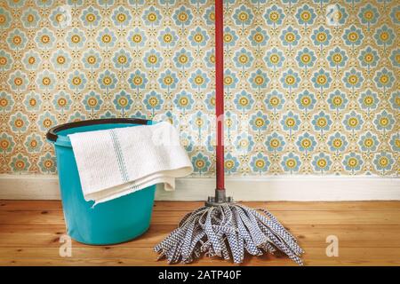 Sepia toned image of a floor mop and bucket in front of retro wallpaper Stock Photo