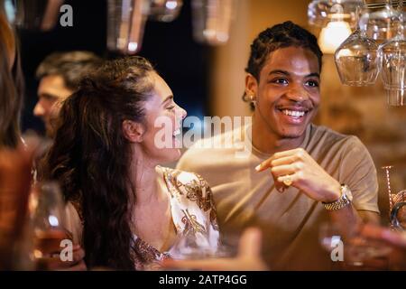 A group of friends laughing with each other at a bar, waiting to order drinks. Stock Photo