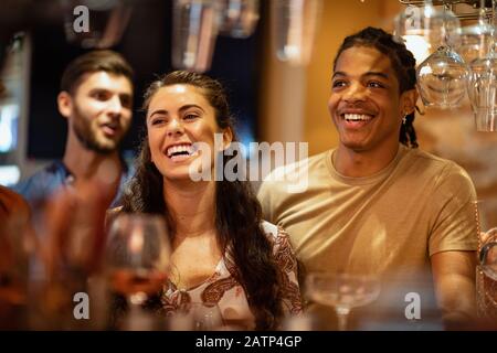 A group of friends laughing with each other at a bar, waiting to order drinks. Stock Photo