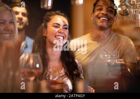 A group of friends laughing with each other at a bar, waiting to order drinks. Stock Photo