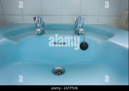 Cold tap left on in tiled bathroom by elderly person forgetful and hence a waste of water and money pouring down the plughole Stock Photo