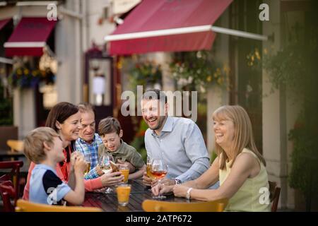 A multi-generation family sitting at a table outdoors at a bar. They are laughing with each other. Stock Photo