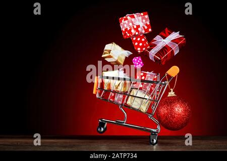 Gift boxes flying out of a shopping cart on red background. Concept of christmas shopping or sale. Stock Photo
