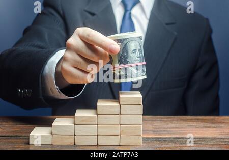 Businessman puts a dollars bundle on top of stairs. Raising bids, increase interest rate deposit account growth. Salary growth and career ladder progr Stock Photo