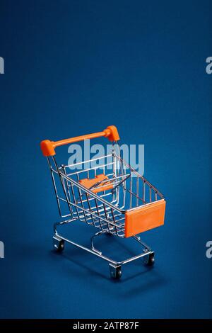 Empty shopping cart trolley on blue background with copy space. Close up. Stock Photo